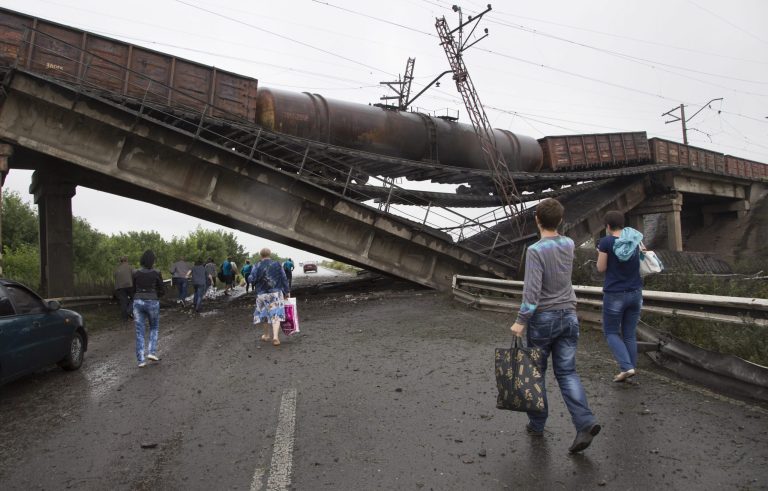 People walk under a destroyed railroad bridge over a main road leading into the east Ukraine city of Donetsk, near the village of Novobakhmutivka,  20 km North from the city of Donetsk, eastern Ukraine Monday, July 7, 2014. The bridge has been destroyed, blocking a key access route to the rebel-held city. (AP Photo/Dmitry Lovetsky)