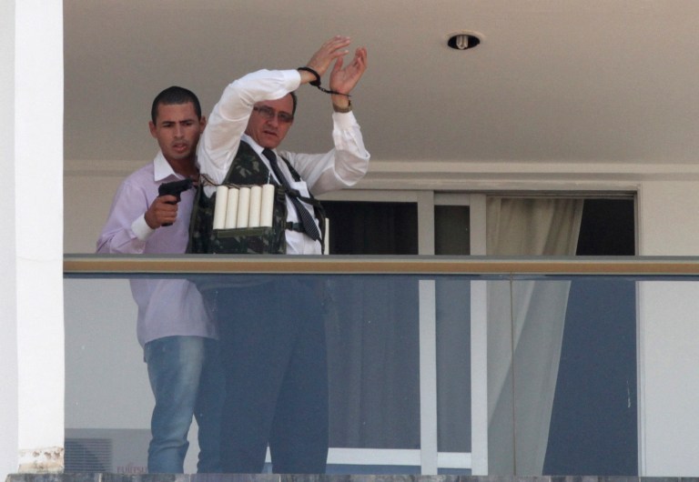 An unidentified man holding what appears to be a gun, parades a handcuffed hostage wearing what appears to be an explosive vest, on the 13th floor balcony of the Saint Peter Hotel, in Brasilia, Brazil, Monday, Sept. 29, 2014. Firefighters and police have cordoned off the area and about 300 guests and other employees left the hotel, some reportedly told to leave by the same man carrying out the attack. Police didn't confirm whether there were actually explosives in the garment. (AP Photo/Eraldo Peres)