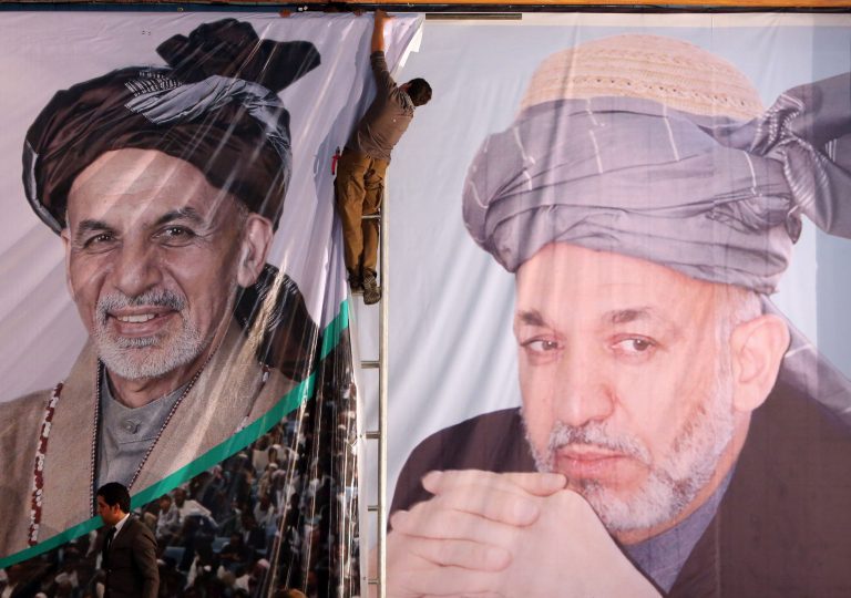An Afghan boy prepares a banner of Afghan president-elect, Ashraf Ghani Ahmadzai, next to a banner of outgoing President Hamid Karzai during his first public appearance since winning the election runoff in Kabul, Afghanistan, Monday, Sept. 22, 2014, Afghanistan's new president-elect says he wants Afghan women represented at the highest levels of government, and he pledged to appoint a woman to the Supreme Court. (AP Photo/Rahmat Gul)