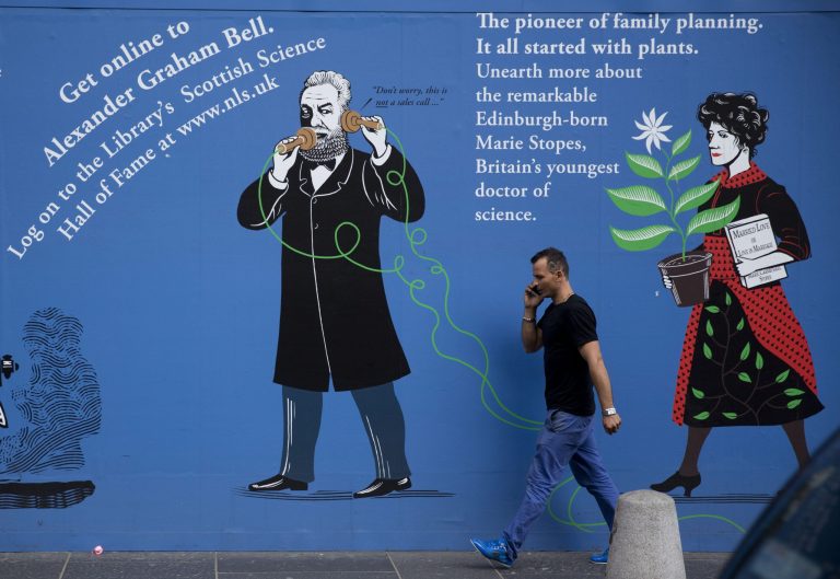 A man talking on a phone walks past images of Scots inventor Alexander Graham Bell  and Scots doctor Marie Stopes outside the National Library of Scotland in Edinburgh, Scotland, Tuesday, Sept. 16, 2014. The land that gave the world haggis and tartan has produced so much more, from golf and television to Dolly the Sheep and 