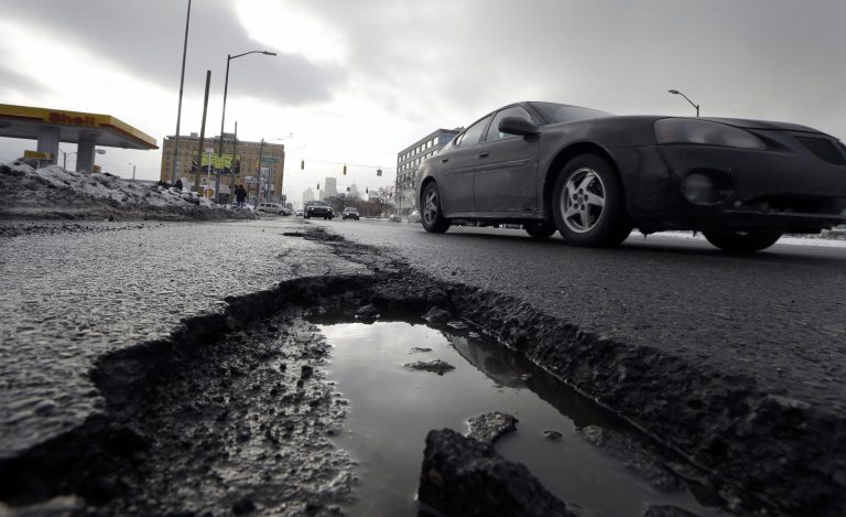 FILE - In this Feb. 11, 2014 file photo a car drives by a pothole in Detroit. The state House's vote to slowly raise gasoline taxes over time if prices increase has senators asking: Is it enough to fix Michigan's deteriorating roads? Talks are underway on whether lawmakers can capitalize on voter anger over shoddy roads and commit to a much higher tax increase, phased in over a handful of years. (AP Photo/Carlos Osorio, File)