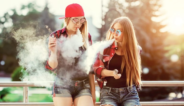 Two young women vaping outdoors.