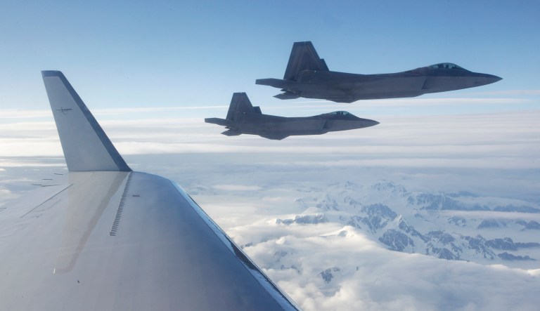 F-22 fighter jets fly off the wing of a civilian airplaneover a mountainous area of Alaska.