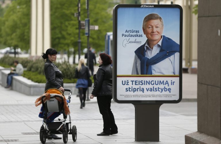 Local residents stand near an election poster showing  Lithuanian Labour Party leader Arturas Paulauskas, a presidential candidate,  in Vilnius, Lithuania, Friday, May 9, 2014.  The poster reads 