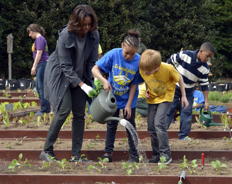 FILE - This April 2, 2014 file photo shows first lady Michelle Obama helping to hold a watering can after she and Friendship Public Charter Elementary School student Dynasty Meade, center, and Bancroft Elementary School student Silas Stutz, right, planted broccoli in the White House Kitchen Garden at the White House in Washington. The White House says tours of Michelle Obama's produce garden will be operating again soon. The tours were grounded after mandatory budget cuts went into effect last year. Public tours of parts of the White House also were halted due to the cuts but resumed after President Barack Obama signed legislation funding government operations. The garden tours are scheduled to resume the week of July 14. They are open to community and school groups that are interested in gardening and healthy eating. (AP Photo/Susan Walsh, File)