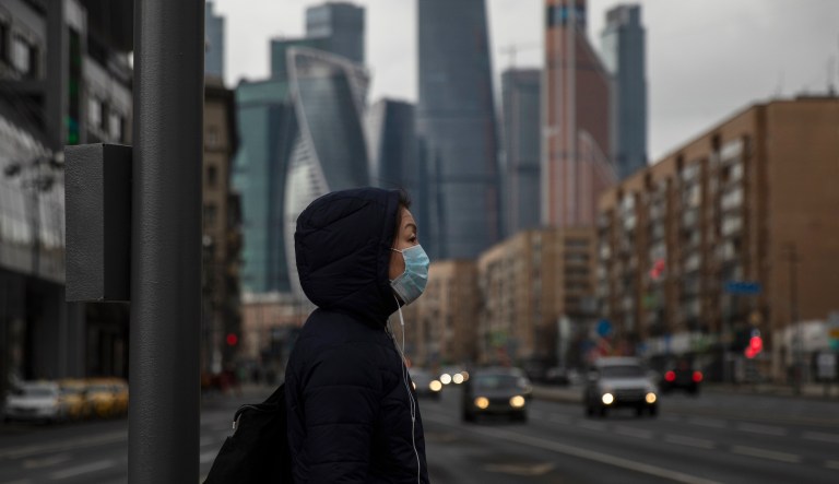 A woman wearing face mask waits to cross a nearly empty road due to residents taking the advice of staying at home to avoid the spread of the coronavirus, with Moscow City skyscrapers in the background, in Moscow, Russia, Thursday, April 2, 2020. Online shopping for food and other supplies has boomed in Moscow after the authorities put most residents on lockdown. The new coronavirus causes mild or moderate symptoms for most people, but for some, especially older adults and people with existing health problems, it can cause more severe illness or death.