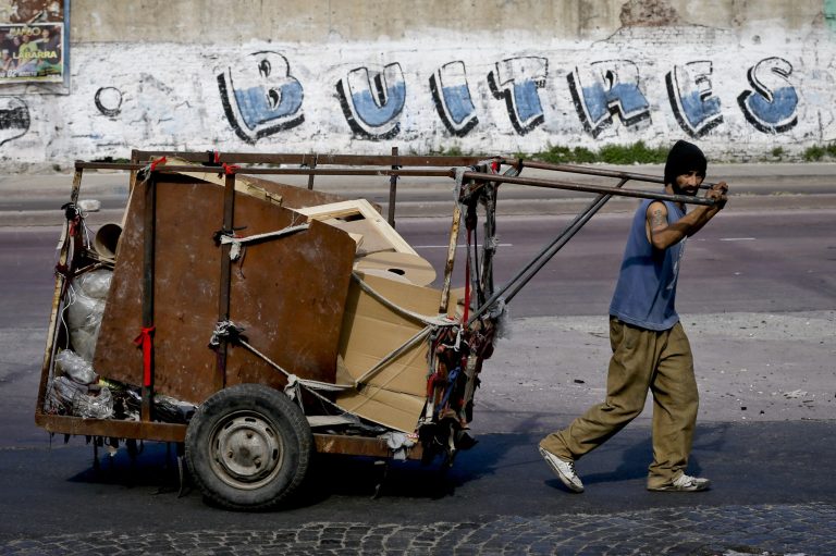 A trash recycler pushes his cart past a sign that reads 