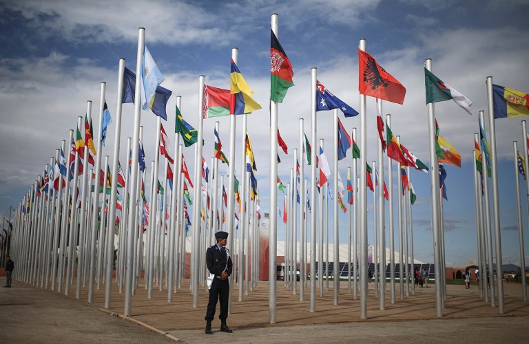 Security stands guard next to flags of participating United Nations member states, on the entrance to the COP22 village in Marrakesh, Morocco. (AP Photo/Mosa'ab Elshamy)