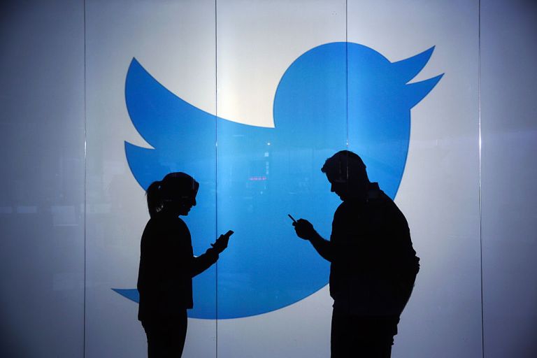 People are seen as silhouettes as they check mobile devices whilst standing against an illuminated wall bearing Twitter Inc.'s logo in this arranged photograph in London, U.K., on Tuesday, Jan. 5, 2016.