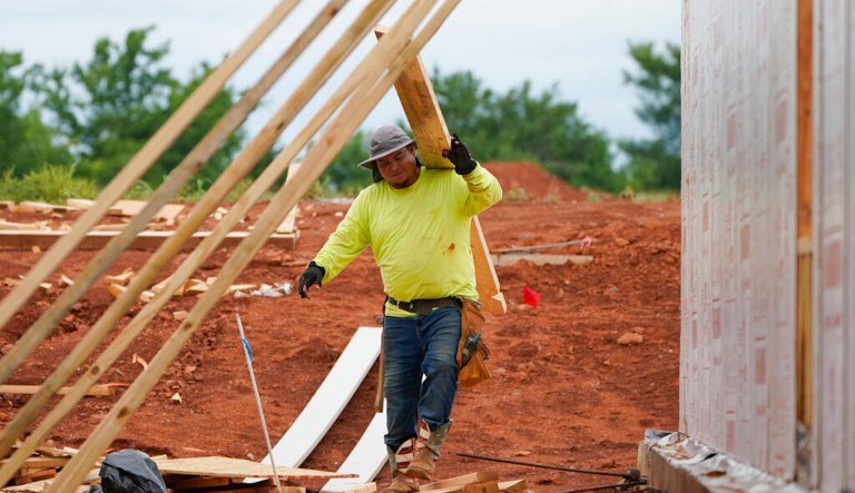 A worker carries a board at a home construction site Tuesday, June 29, 2021, in Piedmont, Okla. The housing market is in decline, raising fears of a broader recession.