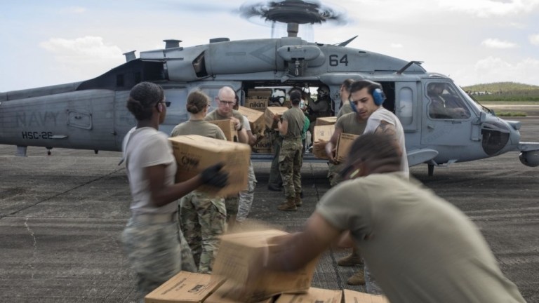 Service members unload food and drinking water from an MH-60S Sea Hawk helicopter embarked aboard the amphibious assault ship USS Kearsarge for distribution to the citizens of Puerto Rico in the aftermath of Hurricane Maria in 2017. 