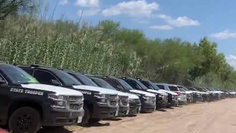 Texas Department of Public Safety vehicles line the dirt road where immigrants were crossing the Rio Grande and walking up to the Del Rio port of entry bridge.