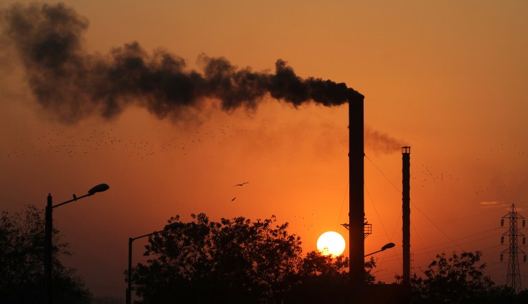 Birds fly past at sun set as smoke emits from a chimney at a factory in Ahmadabad, India, Monday, Dec. 8, 2014.