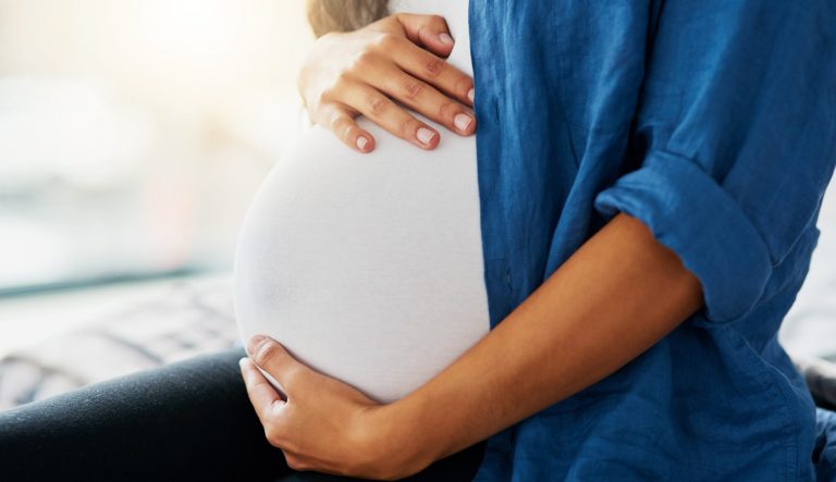 Closeup shot of a pregnant woman holding her belly at home.
