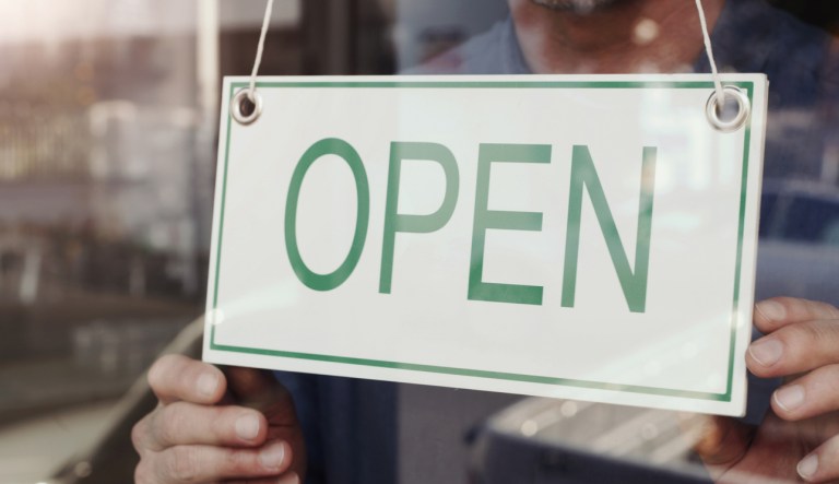 Shot of a shop owner hanging up an "open" sign.