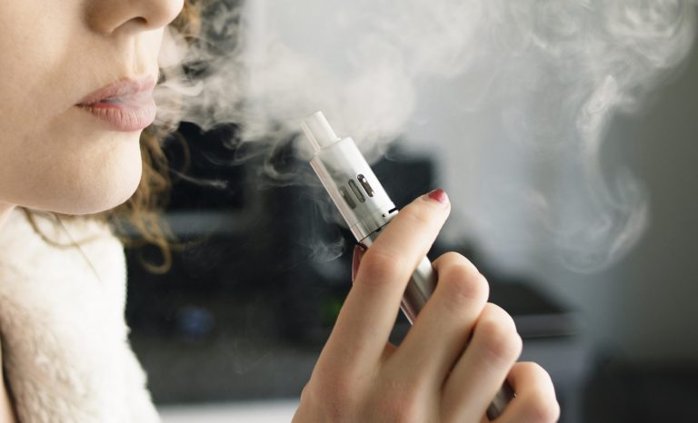 Close-up of a young woman exhaling smoke vapor from an electronic cigarette.