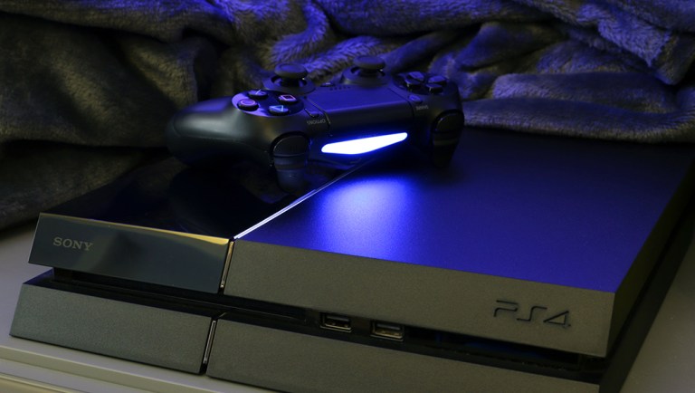 Sony Playstation 4 and black wireless DualShock 4 controller on a desk. The PlayStation 4, registered trademark PLAYSTATION 4 is a video game console produced by Sony Computer Entertainment and is part of the eighth generation of consoles.