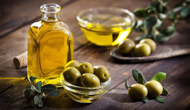 Horizontal shot of an olive oil bottle and a little glass bowl filled with green olives on rustic wood table.
