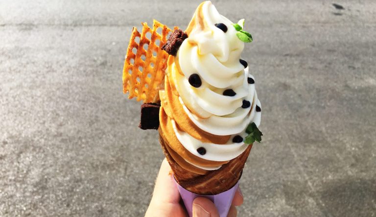 Hand holding gourmet soft-serve ice cream in waffle cone on the city street.