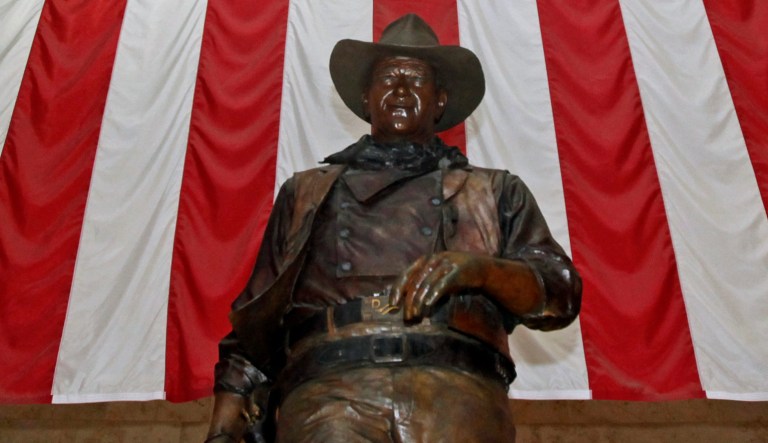 A bronze statue of late actor John Wayne stands before a four-story high American flag at John Wayne Orange County Airport in Santa Ana, Calif.