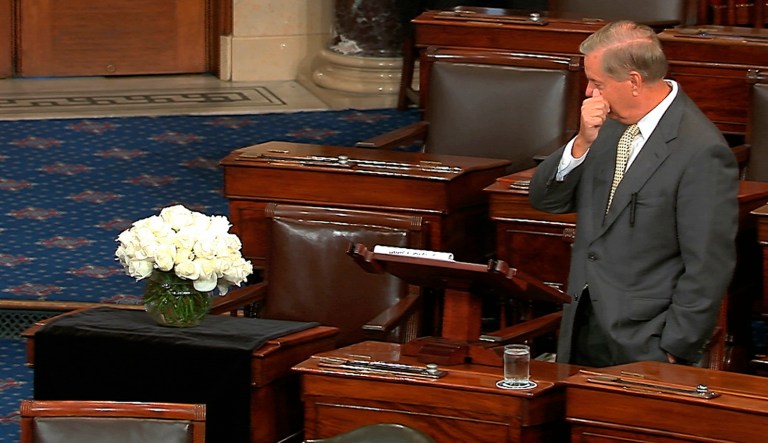 In this image from Senate Television, Sen. Lindsey Graham, R-S.C., pauses as he speaks on the Senate floor at the Capitol in Washington, on Tuesday, Aug. 28, 2018, next to the desk of Sen. John McCain, R-Ariz., draped in black with a bowl of white roses sitting on it. McCain died on Aug. 25, after battling brain cancer. Graham was McCain's best friend in the Senate.