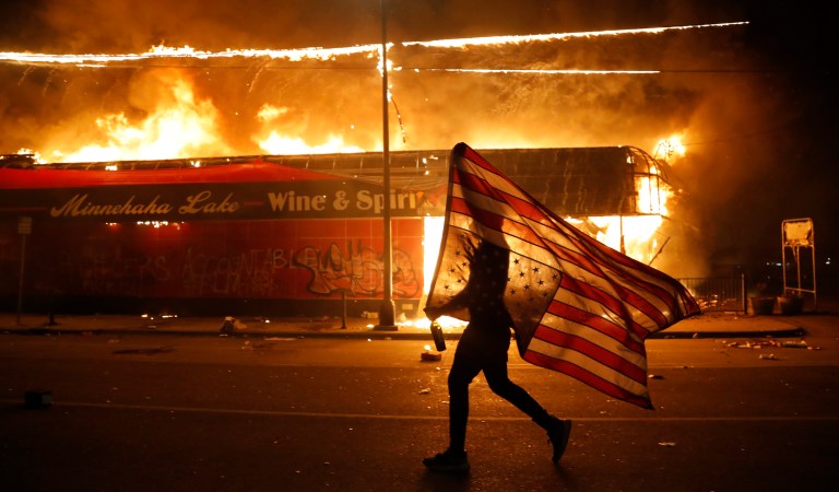 A protester carries the carries the U.S. flag upside, a sign of distress, Thursday, May 28, 2020, in Minneapolis. Violent protests over the death of George Floyd, the black man who died in police custody broke out in Minneapolis for a third straight night.                      