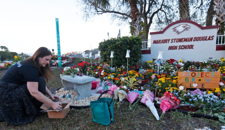 Suzanne Devine Clark, an art teacher at Deerfield Beach Elementary School, places painted stones at a memorial outside Marjory Stoneman Douglas High School during the one-year anniversary of the school shooting, Thursday, Feb. 14, 2019, in Parkland, Fla. A year ago on Thursday, 14 students and three staff members were killed when a gunman opened fire at the high school.
