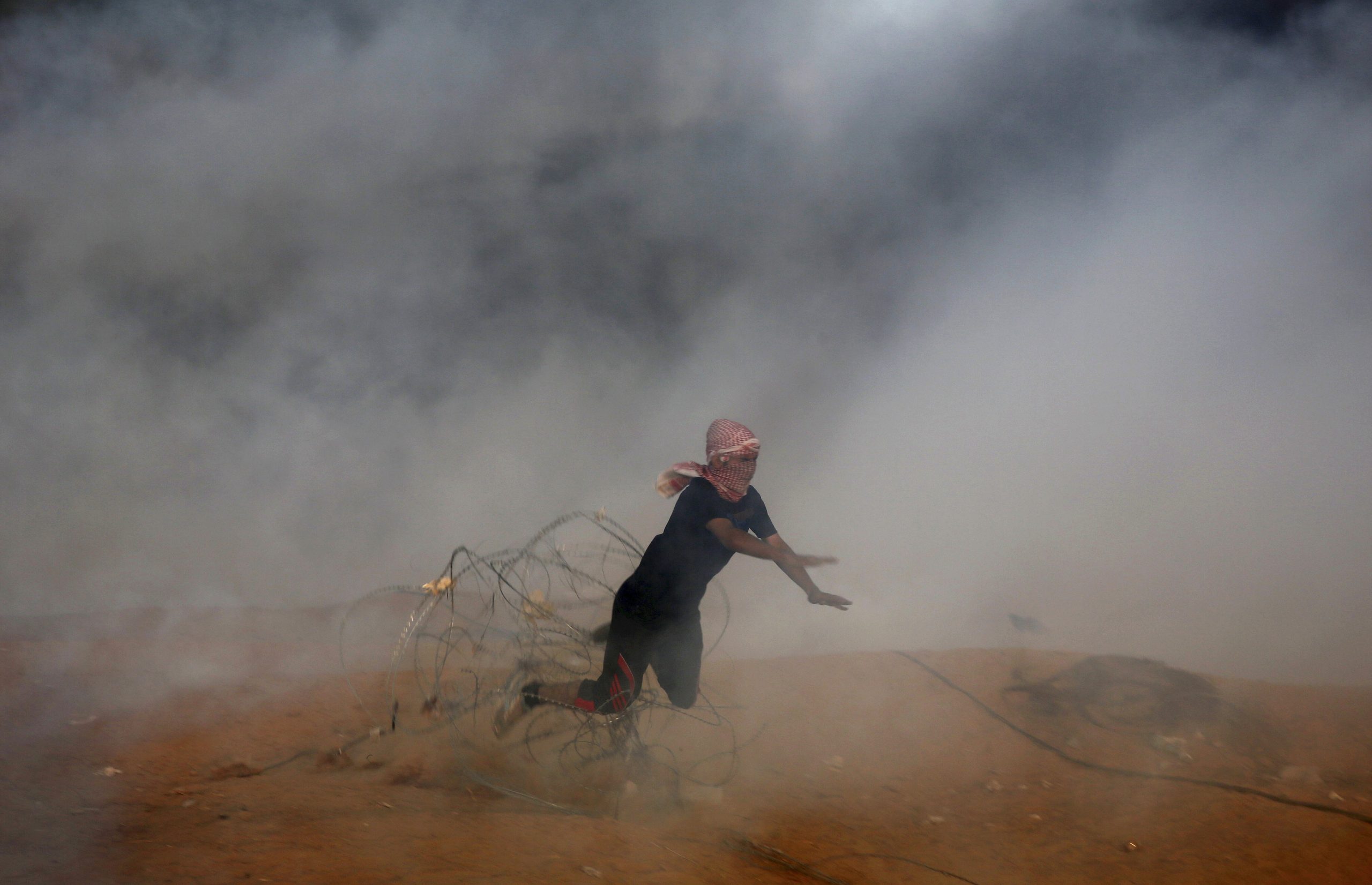A Palestinian protester falls down on a barbed fence as he runs for cover from teargas fired by Israeli troops during a protest east of Khan Younis on Friday. The Israeli military said about 20,000 protesters participated.