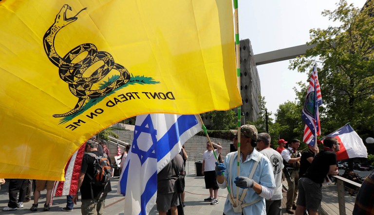 A man standing with members of Patriot Prayer and other groups supporting gun rights holds an Israeli flag and a "Don't Tread on Me" flag during a rally, Saturday, Aug. 18, 2018, at City Hall in Seattle. 