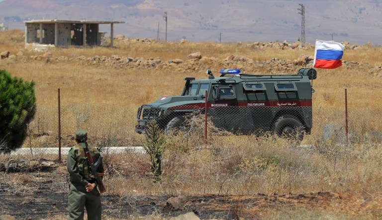 Syrian army soldier stands guard as Russian military police vehicle passes by near the town of Alhureyeh, Syria, Tuesday, Aug. 14, 2018. The Russian military said Tuesday that its forces in Syria will help U.N. peacekeepers fully restore patrols along the frontier with the Israeli-occupied Golan Heights, reflecting Moscow's deepening role in mediating between the decades-old foes.