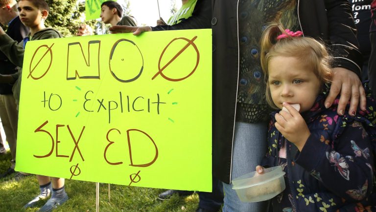 Magdlene Seliuzhytskaya, 2, eats a snack during a rally she attended with her mother, Vicktoryia Seliuzhytskaya, to protest proposed changes to sex education guidance for teachers, Wednesday, May 8, 2019, in Sacramento, Calif. The California State Board of Education is set to vote Wednesday on new guidance for teaching sex education in public schools. The guidance is not mandatory but it gives teachers ideas about how to teach a wide range of health topic including speaking to children about gender identity.