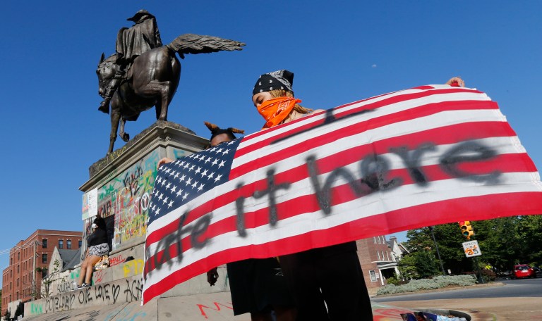 Protester Andie Baker, of Richmond, holds a US flag in front of the graffiti-covered statue of Confederate General J.E.B. Stuart after two previous nights of unrest  due to the death of George Lloyd Sunday, May 31, 2020, in Richmond, Va. Gov. Ralph Northam issued a curfew for this evening.