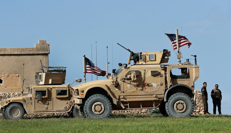 In this picture taken on Thursday, March 29, 2018, a fighter, second from right, of U.S-backed Syrian Manbij Military Council stands next to U.S. humvee at a U.S. troop's outpost on a road leading to the tense front line between Syrian Manbij Military Council fighters and Turkish-backed fighters, at Halawanji village, north of Manbij town, Syria. The front line has grown more tense in recent days as Turkey threatens to advance on the town to clear it of the U.S-backed fighters. U.S troops have increased their patrols in the area, local commanders say, to prevent an outbreak of fighting and to prevent Turkey from advancing on Manbij.