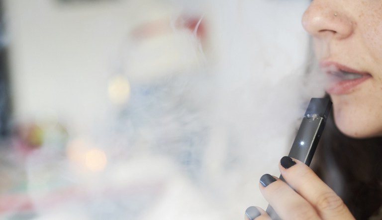 A person smokes a Juul Labs Inc. e-cigarette in this arranged photograph taken in the Brooklyn Borough of New York, U.S., on Sunday July 8, 2018. Juul Labs, the maker of the popular e-cigarette brand that has recently come under fire from health officials over its popularity with young adults, plans to introduce a line of lower-nicotine pods. The company will begin to sell pods with a 3-percent nicotine concentration in its mint and Virginia tobacco flavors later this year, according to a statement Thursday.