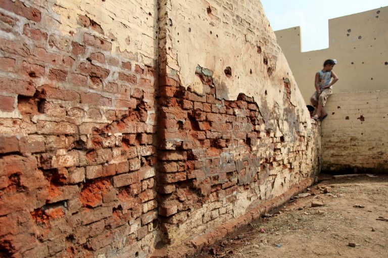 An Indian boy sits on the wall of his house with shell marks allegedly fired from the Pakistan side of the border at Flora village, in Ranbir Singh Pura, 35 kilometers (22 miles) from Jammu, India, Tuesday, Oct. 7. 2014. Indian and Pakistani troops have fired bullets and mortar shells across the border between Kashmir and Pakistan for a second day, with both accusing the other of provoking the violence. (AP Photo/Channi Anand)
