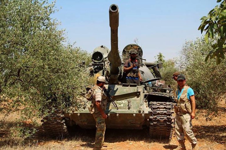 This photo provided by an anti-government activist group Edlib News Network (ENN), which has been authenticated based on its contents and other AP reporting, show Syrian rebels standing next to a tank that was captured from the Syrian government forces at the al-Dahman checkpoint, in southern Idlib, northern Syria, Wednesday, July 9, 2014. Syrian rebels rampaged through a Sunni village in the central province of Hama Wednesday, firing indiscriminately at civilians and killing more than a dozen of people, including seven women, state media and opposition activists said. (AP Photo/Edlib News Network ENN)