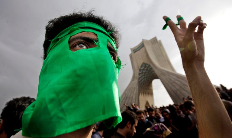 FILE - In this June 15, 2009 file photo, a demonstrator wears a mask in the party's color of green, due to fears of being identified, as hundreds of thousands of supporters of leading opposition presidential candidate Mir Hossein Mousavi, who claims there was voting fraud in election, turn out to protest the result of the election at a mass rally in Azadi (Freedom) square in Tehran, Iran. Despite four years of non-stop arrests and intimidation, Iran's dissidents still find ways to show their resilience. Protest messages ricochet around social media and angry graffiti pops up. But it only takes a closer look at the lockdown atmosphere across Iran ahead of Friday's presidential election to show how much the organized opposition has fallen since massive protests in 2009. ( AP Photo/Ben Curtis, File)