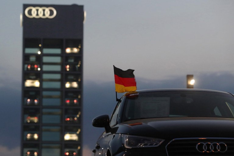 A German national flag flies from an Audi in front of a glass display of new cars at the automaker's Berlin showroom. Audi is among the companies affected by President Trump's proposed tariffs on imports of cars and car parts.