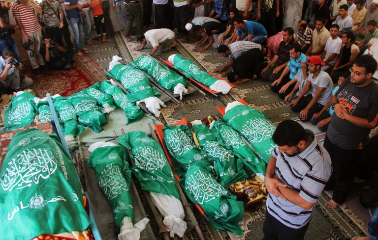 FILE - In this file photo taken Monday, July 21, 2014, Palestinians pray over Hamas flag-draped bodies of 17 members of the Abu Jamea immediate and extended family, killed by an Israeli strike at their house, during their funeral at the main mosque in Khan Younis in the southern Gaza Strip. In the grisly math of the Israel-Hamas war, conflicting counts of combatants and civilians killed in Gaza are emerging - with the ratio perhaps more important to shaping international opinion of the monthlong conflict than any final toll. U.N. researchers and local rights groups say three-fourth of some 1,900 dead were civilians, while the Israeli military estimates the split is closer to 50-50. Those doing the tallies use different methods and standards to make that all important determination of who is a civilian. (AP Photo/Hatem Ali, File)