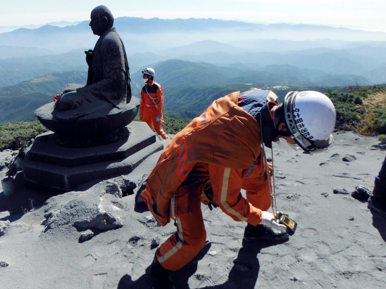 In this Sept. 28, 2014 photo, Nagoya city firefighters uses a gas analyzer to check toxic volcanic fumes next to a Buddha statue on the Mount Ontake in central Japan. Increased seismic activity raised concern Tuesday about the possibility of another eruption at a Japanese volcano where dozens of people were killed, forcing rescuers to suspend plans to try to recover at least two dozen bodies still near the summit. (AP Photo/Nagoya City Fire Dept.) EDITORIAL USE ONLY