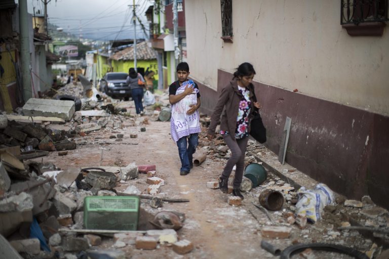 A Family walks trough a street littered with the rubble from buildings that fell during an earthquake in San Pedro, Guatemala, Monday, July 7, 2014. An earthquake measuring 6.9 on the Pacific Coast shook a wide area of ??southern Mexico and Central America Monday. (AP Photo/Luis Soto)