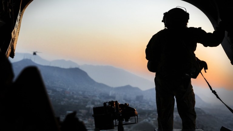 A United States Army loadmaster stands on the rear ramp of a Chinook helicopter and watches the sunset as it flies over Kabul, Afghanistan in September 2017.