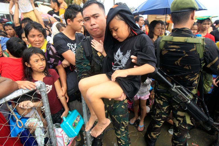 Philippine military personnel attend to children and women first as they wait for evacuation flights in Tacloban, in the central Philippines, on Tuesday. Thousands of typhoon survivors swarmed the airport in an attempt to fly out, but only a few hundred made it, leaving behind a shattered, rain-lashed city short of food and water and littered with countless bodies. (AP Photo/Wally Santana)