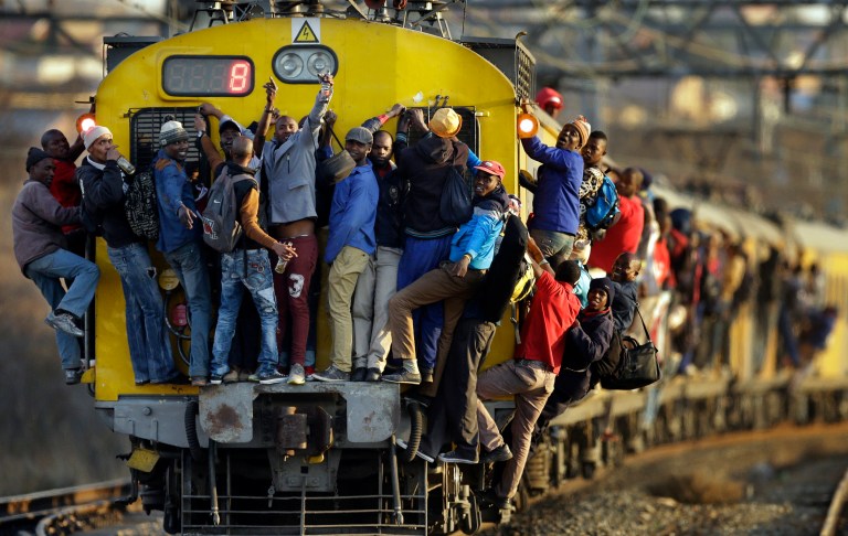 In this Sept. 18, 2014, photo, train commuters hold on to the front and side of an overcrowded passenger train in Soweto, South Africa. (AP Photo/Themba Hadebe)