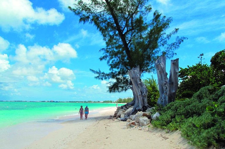 In this Aug. 3, 2012 photo, tourists walk along the beach of Seven Mile Beach in Grand Cayman Island. The Cayman Islands have lost some of their allure by abruptly proposing what amounts to an income tax on expatriate workers who have helped build the territory into one of the most famous or, for some people, notorious offshore banking centers that have tax advantages for foreign investment operations. (AP Photo/David McFadden)