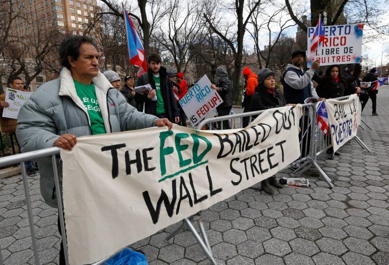 Protesters express their opposition to the fact the the Federal Reserve bank bailed out Wall Street but not Puerto Rico outside International House in New York, where Federal Reserve chair Janet Yellen appeared with former Federal Reserve chairs Ben Bernanke, Paul Volcker and Alan Greenspan. (AP Photo)