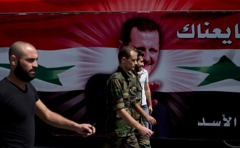 Syrian soldiers walks past a bus with President Bashar Assad's portrait in Damascus, Syria, Tuesday June 3, 2014. Polls opened in government-held areas in Syria amid very tight security Tuesday for the country's presidential election, a vote that President Bashar Assad is widely expected to win. (AP Photo/Dusan Vranic)