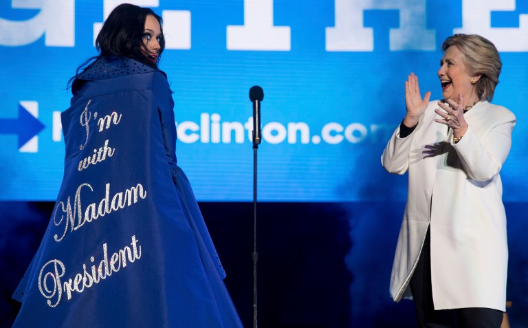 Democratic presidential candidate Hillary Clinton applauds on stage as artist Katy Perry arrives with a cape that reads 