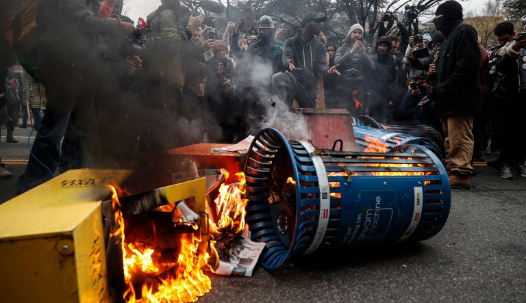 A Washington resident, center right, demands peace as he guards a pile of burning newspaper machines to prevent protestors from feeding the flames during a demonstration after the inauguration of President Trump, Friday, Jan. 20, 2017, in Washington. (AP Photo/John Minchillo)