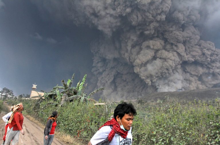 Villagers and a journalist prepare to flee as Mount Sinabung releases pyroclastic flows during an eruption in Namantaran, North Sumatra, Indonesia, Saturday, Feb. 1, 2014. The rumbling volcano in western Indonesia has unleashed fresh clouds of searing gas, killing a number people and injuring fewothers. (AP Photo)